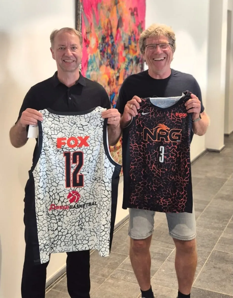 Twee mannen houden ieder een basketbalshirt omhoog, rechts het zwart-oranje wedstrijdshirt van NRG Basketball met het FOX-logo erop